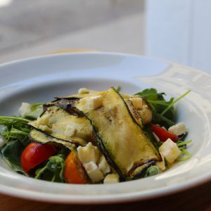 Ensalada de calabacín a la plancha, tomate cherry, queso feta, albahaca, pipas y rúcula