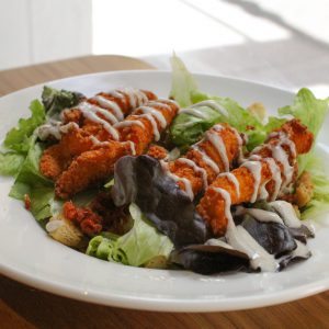 Ensalada César con pollo crujiente, bacon, tomate, y queso parmesano en lascas