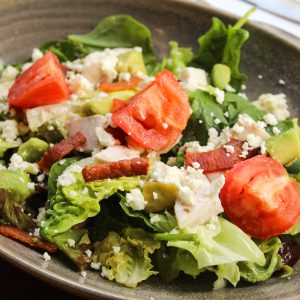 Ensalada de brotes y espinacas con pollo asado, bacon, queso feta y aguacate.